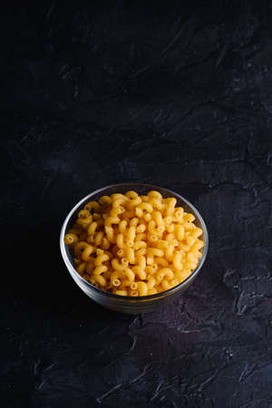 Glass bowl with cavatappi uncooked golden wheat curly pasta on textured dark black background, angle view copy spaceの写真素材