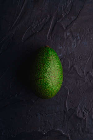 One avocado fruit, fresh ripe organic food on dark black textured background, top viewの写真素材