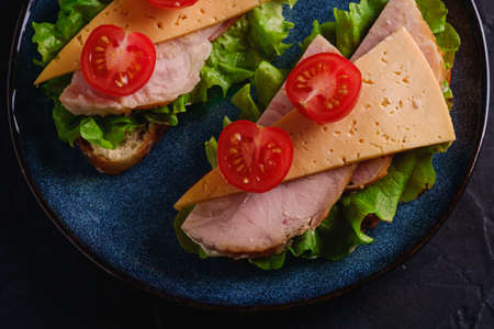 Sandwiches with turkey ham meat, cheese, green salad and fresh cherry tomatoes slices on blue plate, dark textured background, top view macroの写真素材