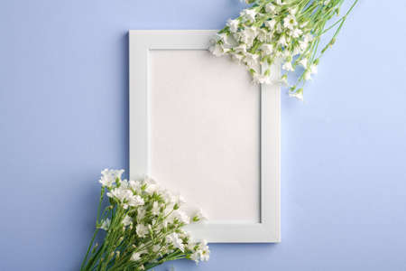 White empty photo frame mockup with mouse-ear chickweed flowers on blue background, top view copy spaceの写真素材