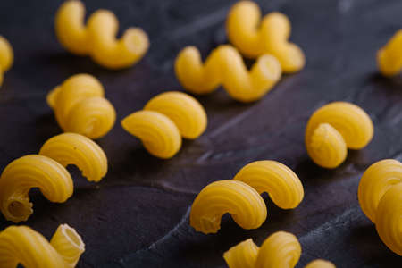 Scattered cavatappi uncooked golden wheat curly pasta on textured dark black background, angle view macroの写真素材