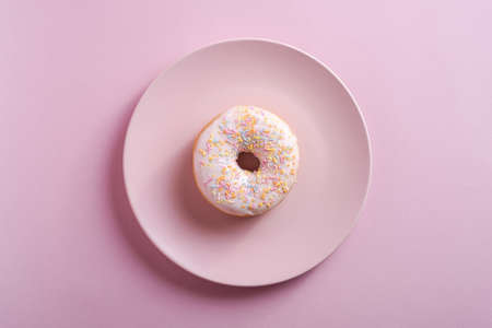 Vanilla donut with sprinkles on pink plate, sweet glazed dessert food on pink minimal background, top viewの写真素材