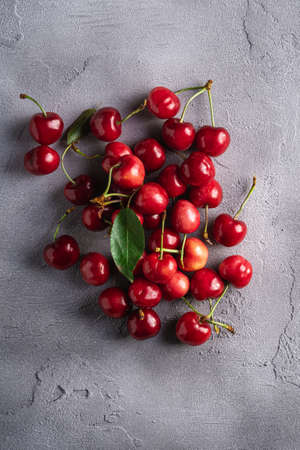 Fresh ripe cherry fruits with green leaves, summer vitamin berries on grey stone background, top viewの写真素材