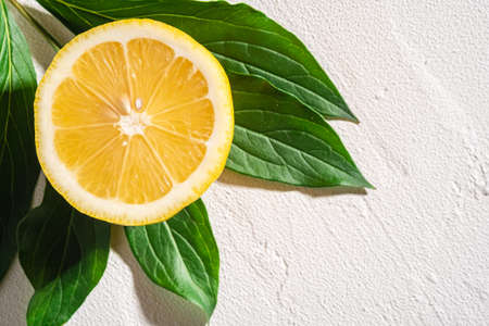 Lemon slice, tropical citrus fruit with green leaves on white concrete background, top view macroの写真素材
