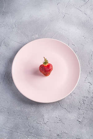 One fresh ripe strawberry fruit in pink plate, summer vitamin berries on grey stone background, top...