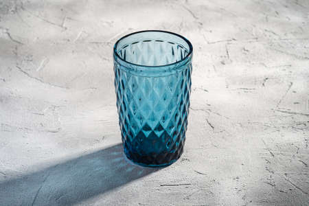 Blue glass geometric cup with colorful shadow light rays on stone concrete background, angle viewの写真素材