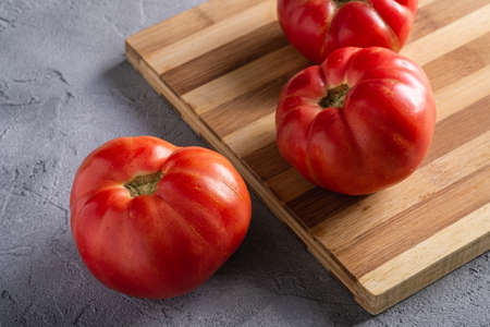 Three pink heirloom tomato vegetables, fresh red ripe tomatoes on wooden cutting board, vegan food, stone concrete background, angle viewの写真素材