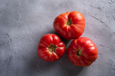 Three pink heirloom tomato vegetables, fresh red ripe tomatoes, vegan food, stone concrete background, top viewの写真素材