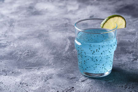 Tasty blue colored cocktail drink with basil chia seeds and citrus lime slice in glass, healthy summer beverage, stone concrete background, angle viewの写真素材