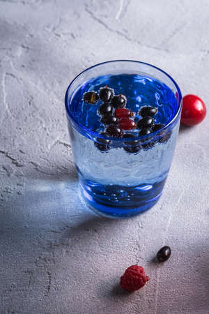 Fresh cold sparkling water drink with cherry, raspberry and currant berries in blue glass on stone concrete background, summer diet beverage, angle viewの写真素材