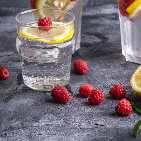 Fresh cold ice water drink with lemon, raspberry fruits and mint leaf in glass on stone concrete background, summer diet beverage, angle view selective focusの写真素材