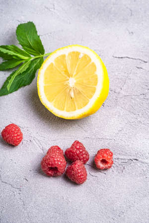 Fresh ripe raspberry fruit with lemon half and mint leaf, summer vitamin red berry and tropical fruit near on stone concrete background, angle view macroの写真素材
