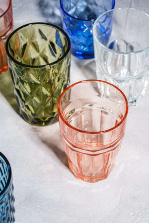Colorful faceted and geometric drink glass, group of empty green, red, blue and transparent drinkware for beverage on stone concrete background, angle viewの写真素材
