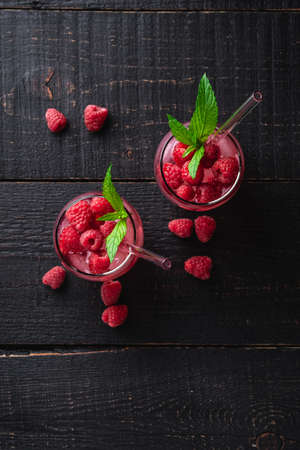 Fresh ice cold berry juice drink with mint, summer raspberry lemonade in two glass with straws on dark wooden background, top viewの写真素材