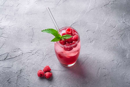 Fresh ice cold berry juice drink with mint, summer raspberry lemonade in glass with straws on stone concrete background, angle viewの写真素材