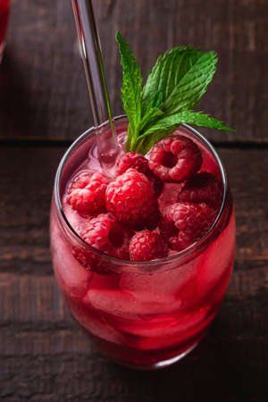 Fresh ice cold berry juice drink with mint, summer raspberry lemonade in glass with straws on brown wooden background, angle view macroの写真素材