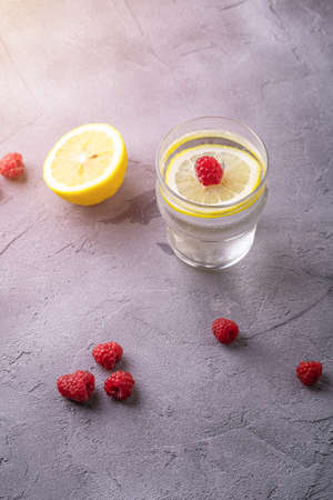 Fresh cold sparkling water drink with lemon, raspberry fruits in glass on stone concrete background, summer diet beverage, angle view selective focusの写真素材