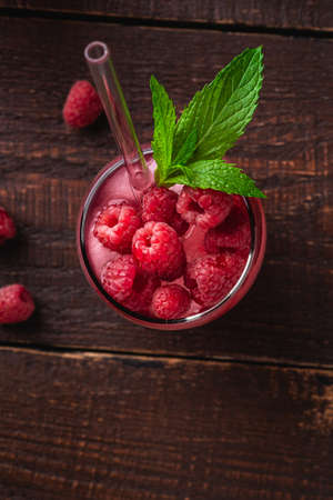 Fresh ice cold berry juice drink with mint, summer raspberry lemonade in glass with straws on brown wooden background, top view macroの写真素材