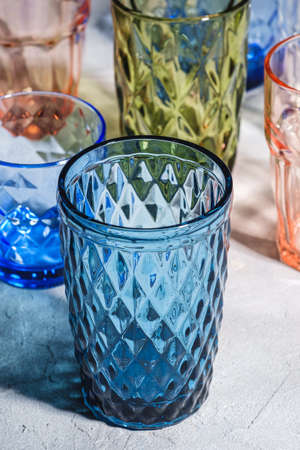 Colorful faceted and geometric drink glass, group of empty green, red, blue and transparent drinkware for beverage on stone concrete background, angle viewの写真素材
