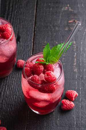 Fresh ice cold berry juice drink with mint, summer raspberry lemonade in two glass with straws on dark wooden background, angle viewの写真素材