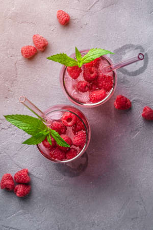 Fresh ice cold berry juice drink with mint, summer raspberry lemonade in two glass with straws on...