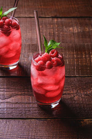 Fresh ice cold berry juice drink with mint, summer raspberry lemonade in two glass with straws on brown wooden background, angle view selective focusの写真素材
