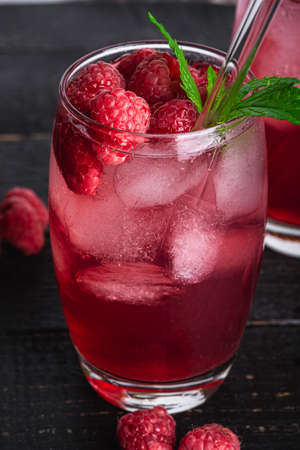 Fresh ice cold berry juice drink with mint, summer raspberry lemonade in glass with straws on dark...