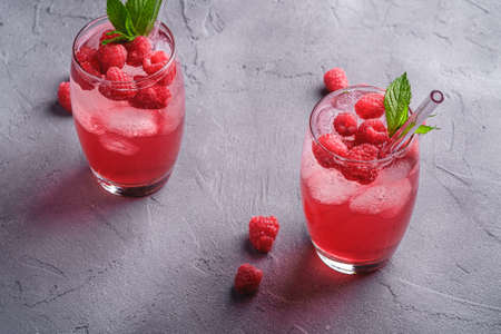 Fresh ice cold berry juice drink with mint, summer raspberry lemonade in two glass with straws on stone concrete background, angle viewの写真素材