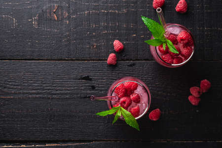 Fresh ice cold berry juice drink with mint, summer raspberry lemonade in two glass with straws on dark wooden background, top view copy spaceの写真素材