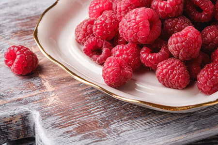 Raspberry fruits in plate on old cutting board, healthy pile of summer berries on grey wooden background, angle view macroの写真素材