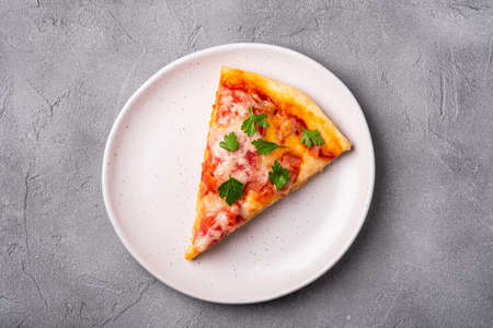 Hot pizza slice with mozzarella cheese, ham, tomato and parsley on plate, stone concrete background,...