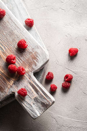 Raspberry fruits on old wooden cutting board, healthy pile of summer berries on stone concrete background, top viewの写真素材
