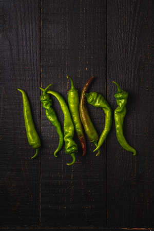 Hot spicy green chili peppers on dark wooden backdrop background, top viewの写真素材