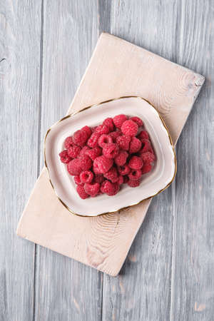 Raspberry fruits in plate on old cutting board, healthy pile of summer berries on grey wooden background, top viewの写真素材