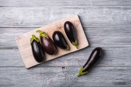 Fresh ripe eggplant on wooden cutting board, grey wood backdrop background, top viewの写真素材