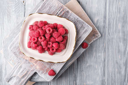 Raspberry fruits in plate on old cutting boards, healthy pile of summer berries on grey wooden background, top viewの写真素材