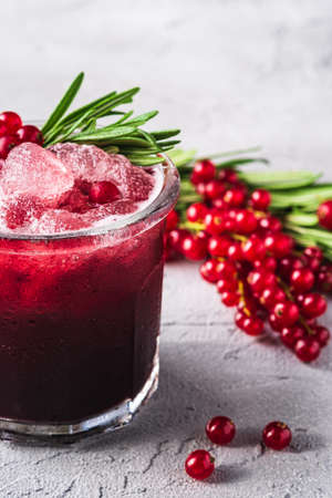 Fresh ice cold fruit cocktail in glass, refreshing summer red currant berry drink with rosemary leaf on stone concrete background, angle viewの写真素材