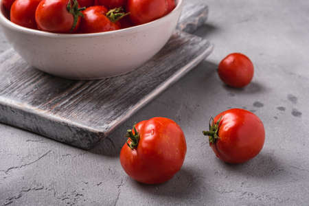 Fresh ripe tomatoes with water drops in bowl on old wooden cutting board, stone concrete background, angle view macroの写真素材