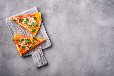 Hot pizza slices with mozzarella cheese, ham, tomato and parsley on wooden cutting board, stone...