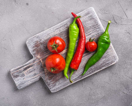 Fresh ripe tomatoes with hot chili peppers on old wooden cutting board , stone concrete background, top viewの写真素材