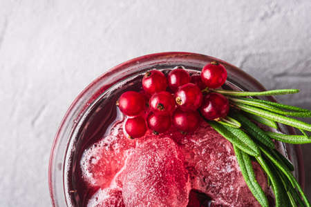 Fresh ice cold fruit cocktail in glass, refreshing summer red currant berry drink with rosemary leaf on stone concrete background, top view macroの写真素材