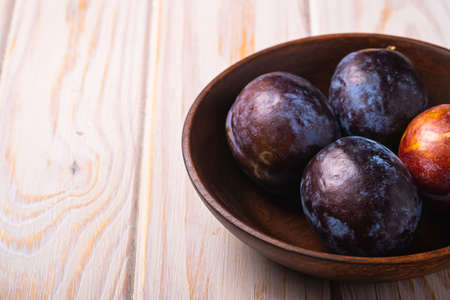 Fresh sweet plum fruits in brown wooden bowl, wood table background, angle view macroの写真素材
