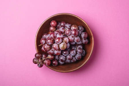 Fresh ripe grape berries in brown wooden bowl on pink minimal background, top viewの写真素材