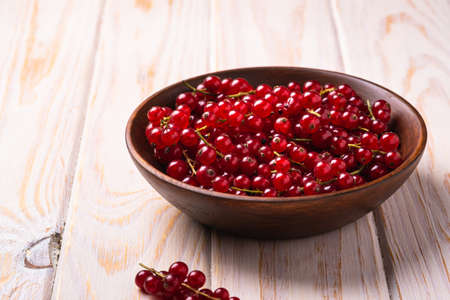 Fresh sweet red currant berries in wooden bowl, wood table background, angle viewの写真素材