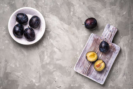Fresh ripe plum fruits whole and sliced in bowl and on wooden cutting board, stone concrete background, top view copy spaceの写真素材