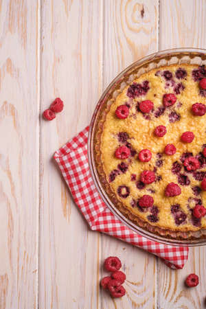 Sweet tasty pie with jellied and fresh raspberry fruits in baking dish with red tablecloth towel, wooden table background, top viewの写真素材