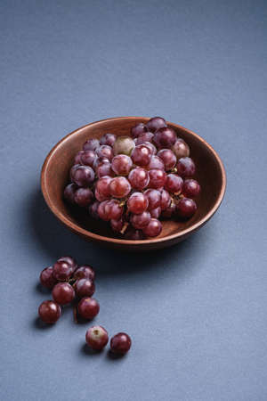 Fresh ripe grape berries in brown wooden bowl on blue grey minimal background, angle viewの写真素材