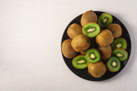Kiwi fruits half sliced in black plate on vibrant plain white background, copy space, top viewの写真素材