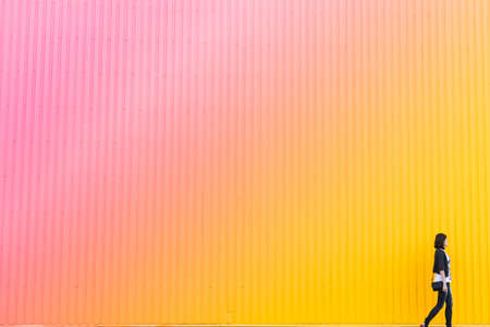 Woman walks near colorful pink and yellow wall, copy space backgroundの写真素材