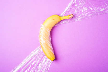 Banana fruit wrapped in stretch wrap plastic on pink background, minimalistic creative layout, ecology and environment conceptの写真素材